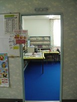 入口の先に青いカーペット敷かれ本棚やテーブルが設置されている部屋の様子を廊下から撮った写真