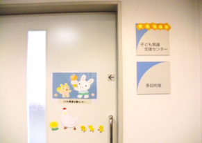 ドアにウサギやリス、ニワトリやヒヨコのイラストが描かれている子育て支援センター入口の写真