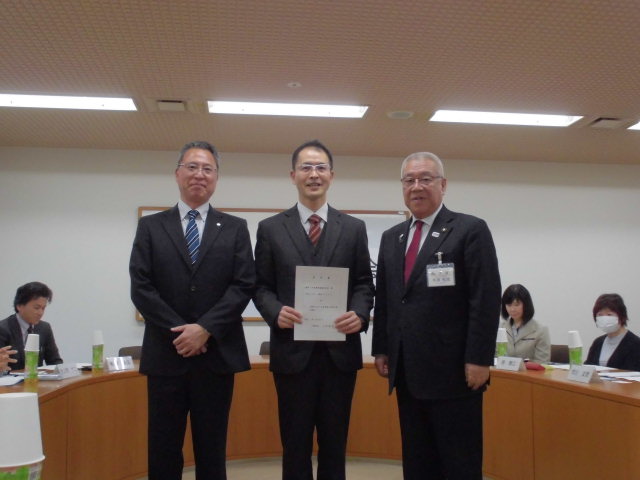 右側に木津市長、中央に諮問書を持っている男性、左側に手を前に組んで立っている男性3名が並んで立っている写真
