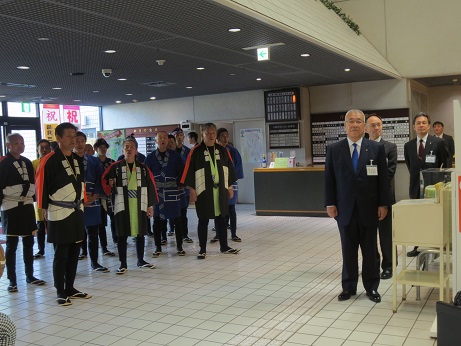 市民ホールのロビーの左側に木遣唄の披露を行っている鳶組合の皆さんが立ち、右側に市長と他2名の男性が立っている写真