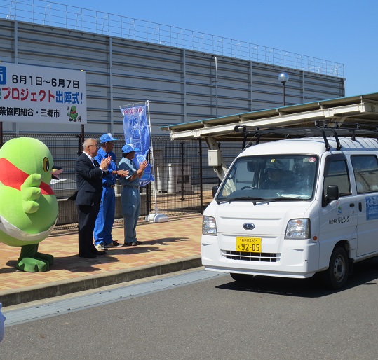マスコットキャラクターかいちゃんや市長、2名の関係者が、社用車で出発する方々を拍手して見送っている様子の写真