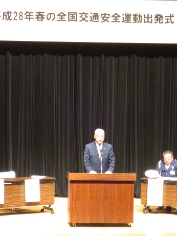 「平成28年春の全国交通安全運動出発式」と書かれたステージの演壇で挨拶を行っている市長の写真