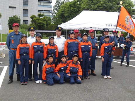 前列に3名後列に6名の少年消防クラブの皆さんが並び、最後列に4名の消防団の男性と市長と市長と同じ制服を着た男性が並んでいる記念写真