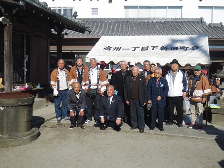「高洲一丁目下新田町会」と書かれた白いバザーテントの前で、三郷市長が町会のメンバーと集まり記念撮影をしている写真