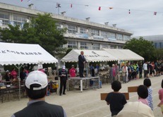 校舎の前にテントが並び、朝礼台の上に立つ市長が挨拶を行っている高州・東町地区の体育祭の様子の写真