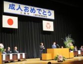 成人式式典会場のステージの檀上で、スーツ姿の男性が二十歳の主張を行っている様子を左斜めから撮影した写真