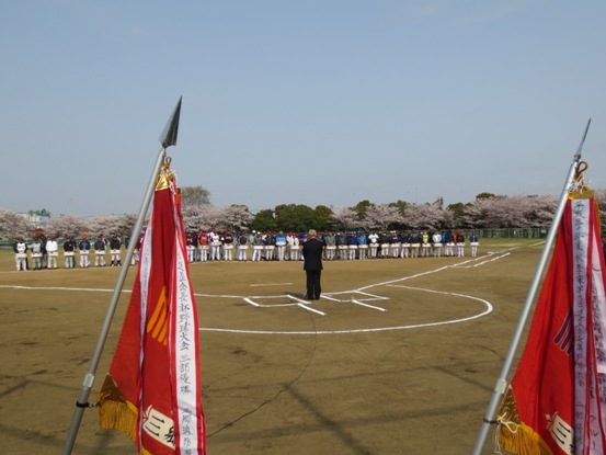 白線が引かれたバッターボックスに立つ市長が、横並びに立つ多くの参加チームのかたと向かい合っており、手前には優勝旗が立てられている写真