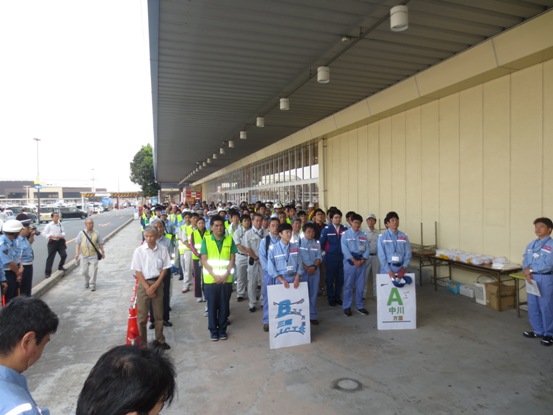 作業着や反射ベストを着用した主催者と200名を超える道路関係団体のメンバーがピアラシティ横のスペースに整列し、最前列の2名がそれぞれ「A中川方面」「B三郷JCT方面」と書かれたボードを持っている写真