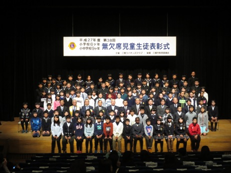 ステージ上に表彰された子供たちや胸章リボンをつけた関係者、南中学校の吹奏楽部の皆さんが並んでいる記念写真