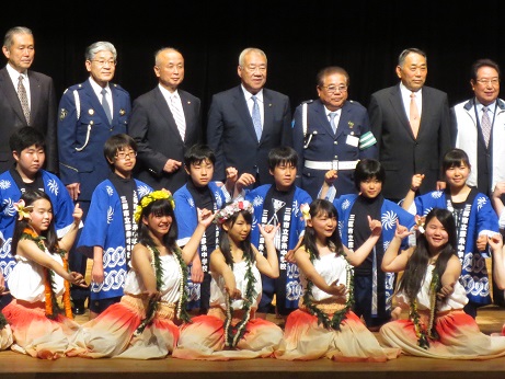 手前に白色とオレンジ色の衣装を身にまとった5名の女の子、2列目に法被を着用した6名の彦糸中地域貢献部の皆さん、後列に市長を中央に6名の関係者が立っている記念写真