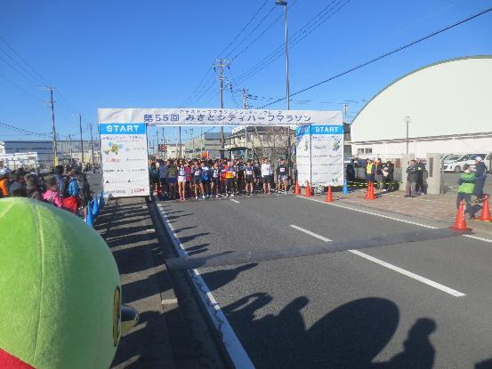左手前に市のマスコットキャラクターかいちゃんが見守る中、ランニングウェアを着たたくさんのランナーが、スタート地点についている写真