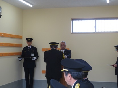 制服を着用した消防団員と市長が向かい合って立ち引渡式を行っている様子の写真