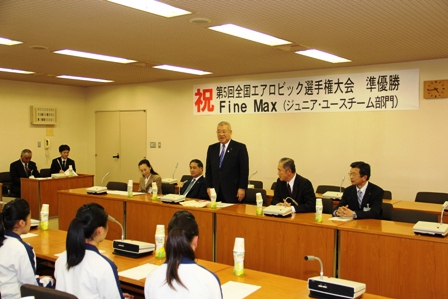 「祝第5回全国エアロビック選手権大会準優勝Fine Max（ジュニア・ユースチーム部門）」と書かれた横幕が壁に貼られた室内で、ファインマックスの方々と4名の職員が向かい合って座り、中央の席の市長が席から立ち話をしている写真