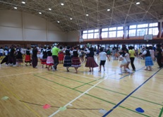 ハンガリー風のフォークダンスの衣装を着た方々が手をつないで体育館いっぱいに広がってダンスを行っている様子の写真