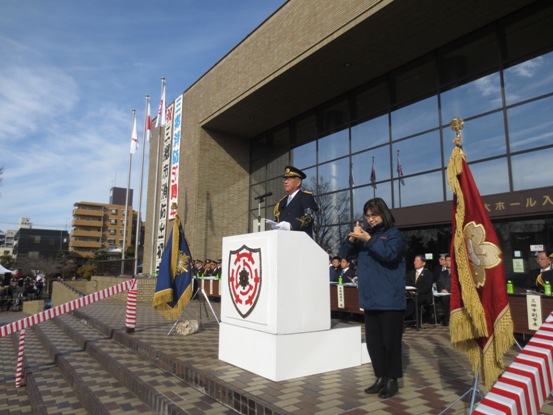 文化会館の建物入り口前に演台が置かれ、制帽を被った市長が演台に立って話をしている写真