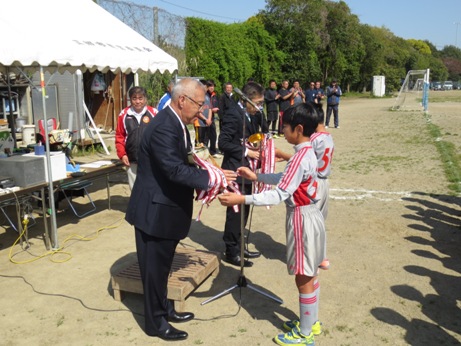 グレーのユニフォームを着た子どもたちが三郷市長と関係者の男性に市長杯を返還している様子の写真