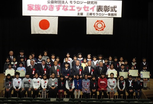 ステージの上に市長をはじめ胸章リボンをつけた関係者や受賞した子供たちが並んでいる記念写真