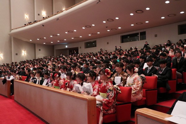 会場の客席が、振袖やスーツ姿の新成人たちで満席になっている写真