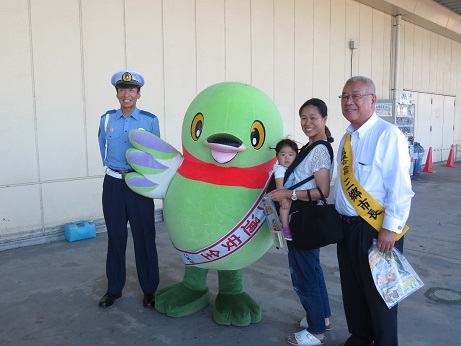 三郷市長と警察官、女の子を抱っこ紐で抱っこしているお母さんが、「交通安全」と書かれたタスキをかけているかいちゃんとともに記念撮影をしている写真