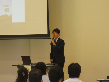 スクリーンに映し出された内容について講演を行う気象予報士の藤富郷さんと、座って話を聞く参加者の写真