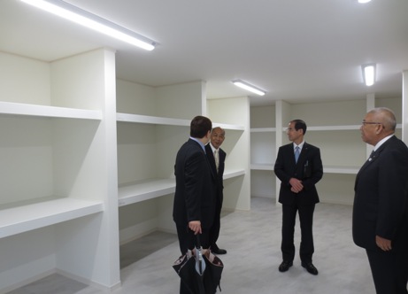 三郷市長が3名の男性とともに白い棚が壁一面に設置されている部屋を内覧している様子の写真