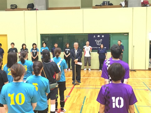 前に立って開会のあいさつをする三郷市長と、チームごとに整列し立って話を聞く水色と紫のユニフォームを着用した参加者の写真
