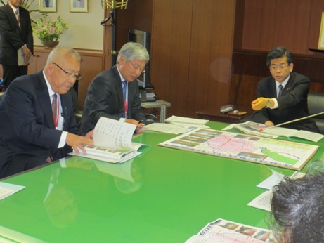 奥の席に座った石井国土交通大臣が大きなテーブルに置かれた資料を指さし、左側に座っている市長が資料をめくり、要望の説明を行っている様子の写真
