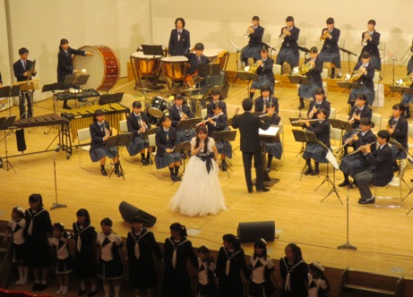 吹奏楽部のステージ演奏に合わせて、白色のドレスを着た井上あずみさんが一緒に歌を歌っているステージの写真