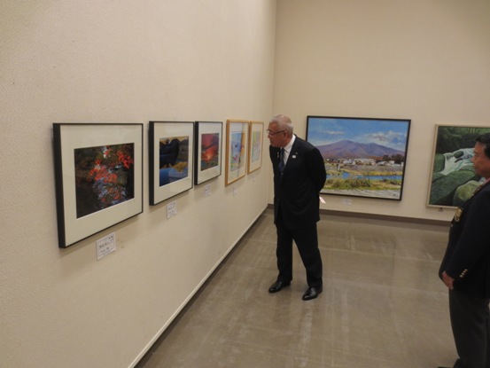 壁に多くの絵画作品が展示されている部屋で、一つの作品に近寄って眺めている市長の写真