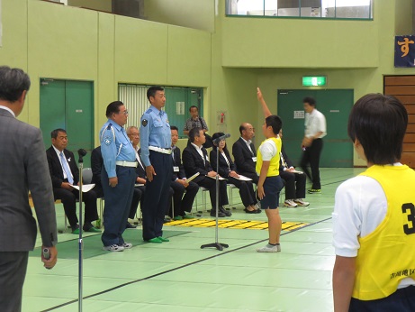 2名の警察官に向かって選手宣誓をする黄色いゼッケンを着用した戸ヶ崎小学校の代表生徒と、その様子を見守るパイプ椅子に座った三郷市長と関係者の写真
