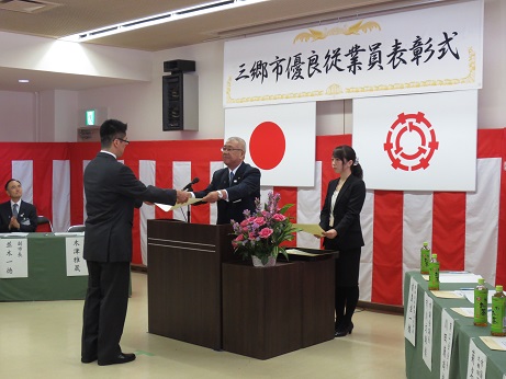 演壇を挟んでスーツ姿の男性と市長が向かい合って立ち表彰を行っている様子の写真