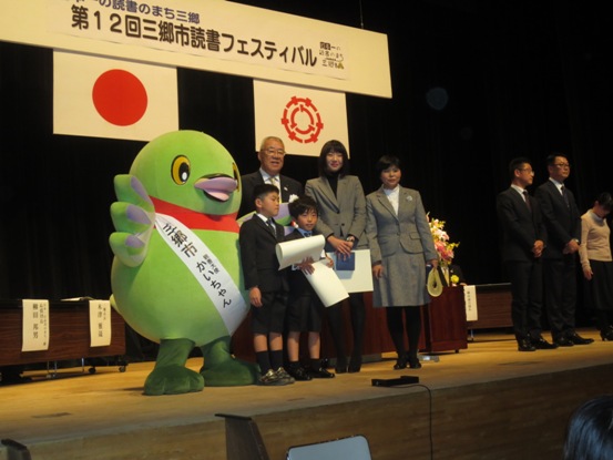 舞台上に4名の受賞者が集まり市長やかいちゃんと一緒に並んで記念撮影をしている写真
