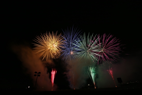黄色・青・緑・ピンクの華麗で大きな花火が夜空に打ちあがっている様子の写真