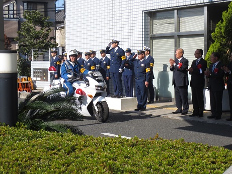 胸章リボンをつけた市長や関係者、敬礼を行っている警察官の方々が見守るなか、白バイに乗った隊員が取締りに出発していく様子の写真
