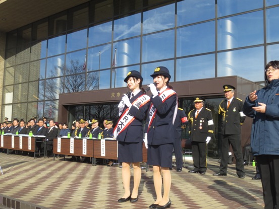 三郷市PR大使のタスキを掛けた「Mika+Rika」さんが制服を着てマイクを手に話をしている写真