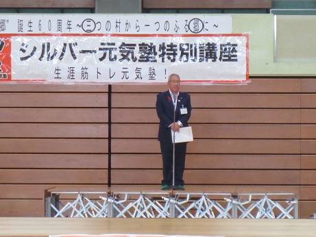 「シルバー元気塾特別講座」と書かれた横幕の下の特設ステージに市長が立ち挨拶を行っている様子の写真