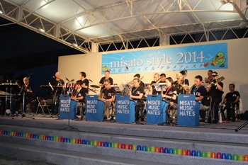 「misato style 2014」と書かれたステージ上で黒色のシャツを着たミサトミュージックメイツオーケストラのメンバーが演奏を行っている様子の写真