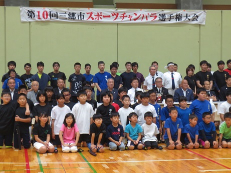 「第10回三郷市スポーツチャンバラ選手権大会」と書かれた横断幕が掛けられている壁の前で、三郷市長と大勢の選手の子どもたち、関係者が集まって記念撮影をしている写真