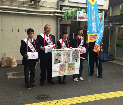 赤色のリボンをつけた募金箱を首にかけた市長と3名の生徒が横一列に並び募金活動を行っている様子の写真