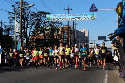 「みさとシティハーフマラソン」と書かれた横断幕の下、路上を走っている参加者の写真