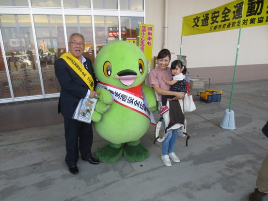 小さな女の子を抱っこした母親とマスコットキャラクターかいちゃんと市長が横一列に並んでいる写真