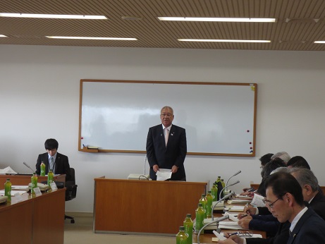 ホワイトボードの前に設置された演台前で話をしている三郷市長と、マイクと飲み物が置かれた席に参加者が座り資料などを見ている様子の写真