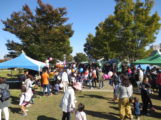 並木道には色々な屋台のテントやのぼり旗が立ち並び、色とりどりの風船を手に持った子どもたち、多くのお客さんで賑わっている会場の様子の写真