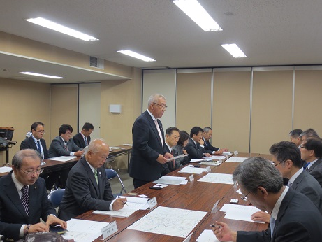 長机が並んだ席に県の関係者や市の担当者が向かい合って座り、中央の席から立ち上がった市長が説明を行っている様子の写真