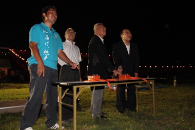 市川商工会青年部長の男性がオレンジ色の点火器を指さし、川田商工会長が夜空を見上げ、木津市長と篠田市議会議長が夜空を見上げながら点火を行っている点火式の様子の写真
