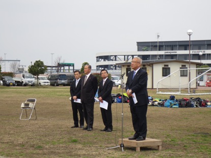 左側に3名のスーツを着た男性が横一列に並び、手前に設置された小さな台の上に立って挨拶を行っている市長の写真