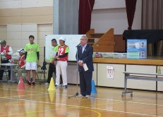 体育館のステージ左下にスタッフが立ち、中央に設置されたマイクスタンドの前に立つ市長が挨拶を行っている東和地区の体育祭の様子の写真