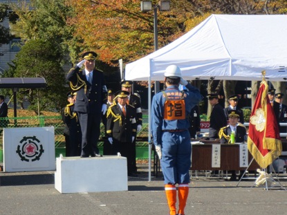 ヘルメットを被り作業着を着た消防団員と向かい合って小さな台の上に乗っている市長が敬礼をしている様子の写真