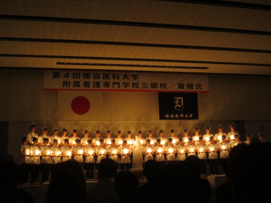 照明が落とされ戴帽生が横2列に並び、中央に設置されたナイチンゲール像が携えたキャンドルから引き継ぎ灯されたキャンドルを持っている様子の写真