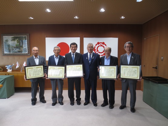 国旗と三郷市旗が飾られた室内で、市長を中央に額入りの感謝状を持った5名の方々が横一列に並んでいる写真